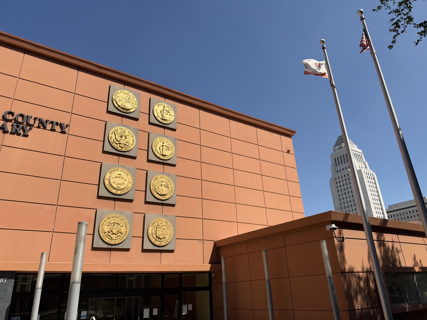 Gold seals of the California Supreme Court, the Ninth Circuit, the Superior Court of Los Angeles County and other courts on the Law Library facade, with Los Angeles City Hall rising behind the flagpoles