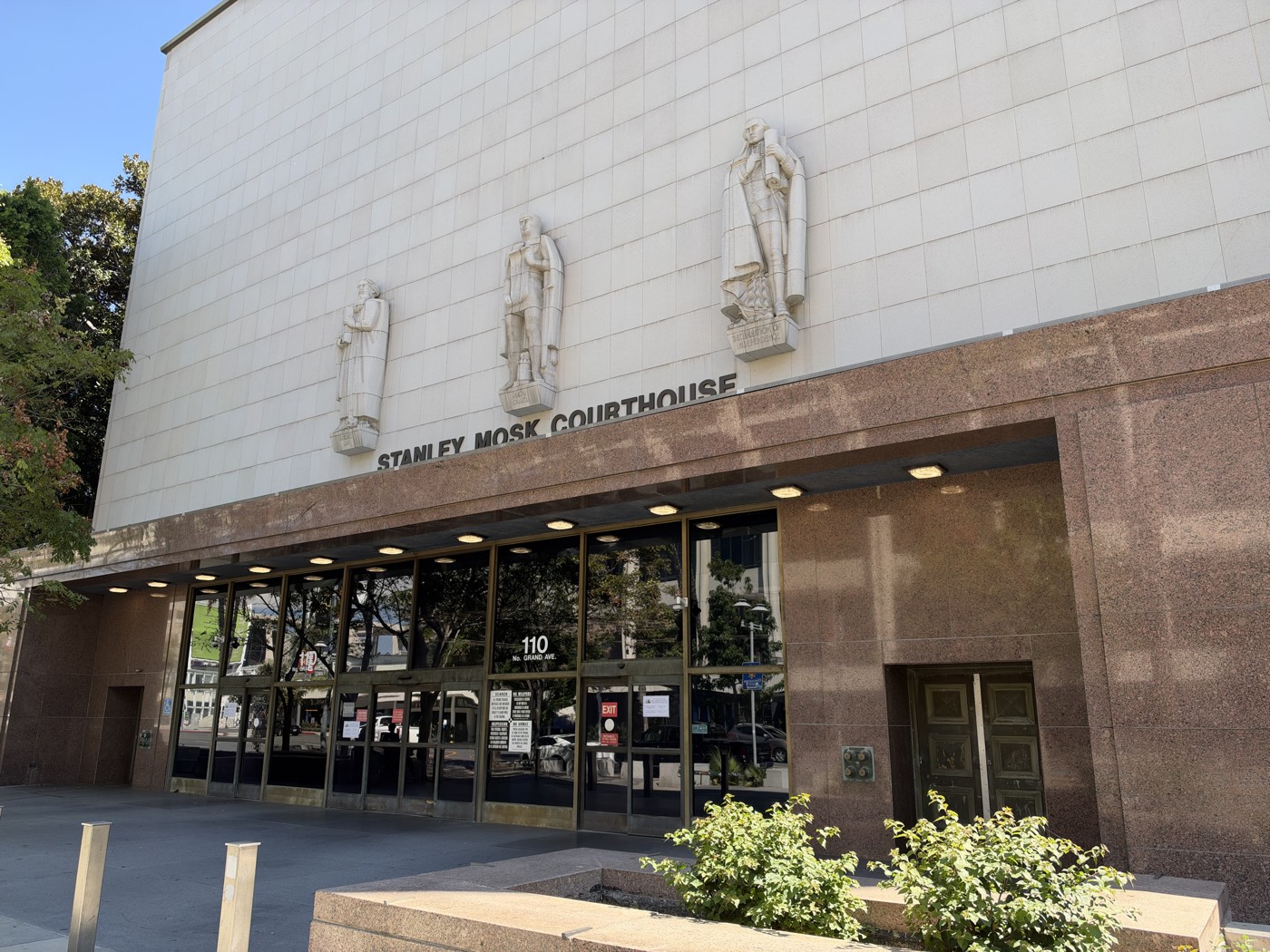 The Grand Avenue entrance of the Stanley Mosk Courthouse in downtown Los Angeles, with the building&rsquo;s name and three carved figures above the doors